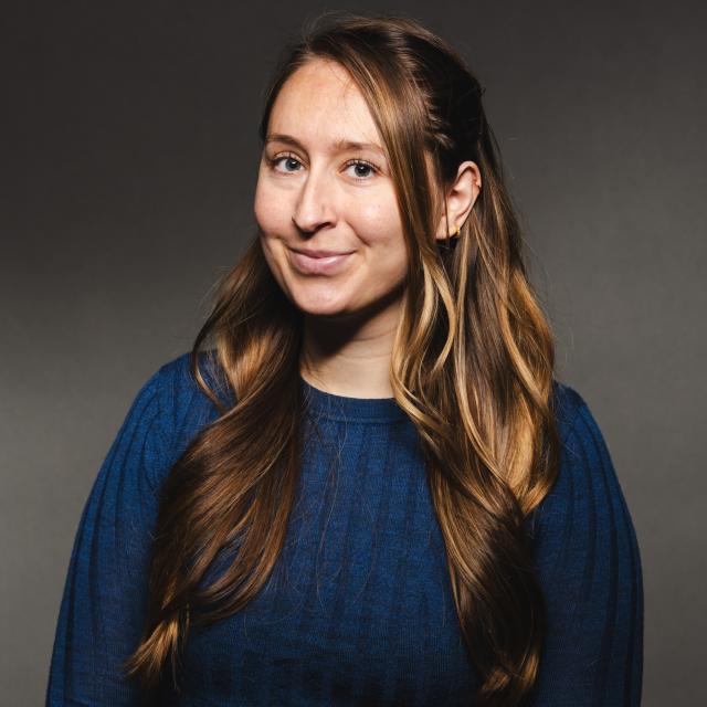 Angela Chesler wearing a blue shirt smiling for her headshot with a black background.